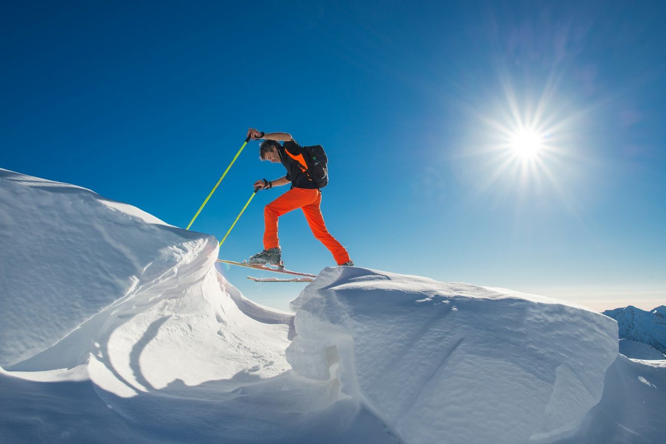 title Skifahrer in orangefarbenen Hosen über schneebedeckte Kante unter klarem Himmel.
